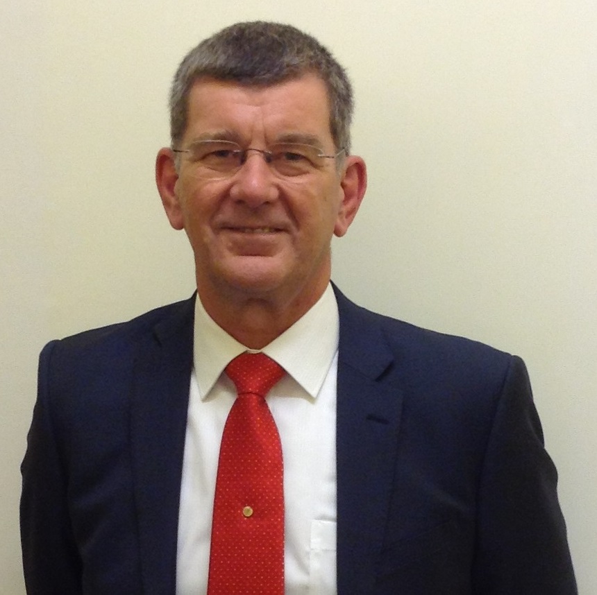  A picture of the Chair of Governors, Bradley Jones. He is a white male, over 60 years old with short grey hair, a navy suit jacket and white shirt with a red tie