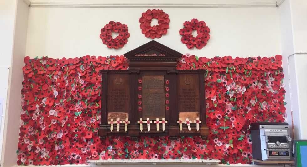  A World War 1 memorial in the school hall, surrounded by hundreds of red  poppies that the children have made.