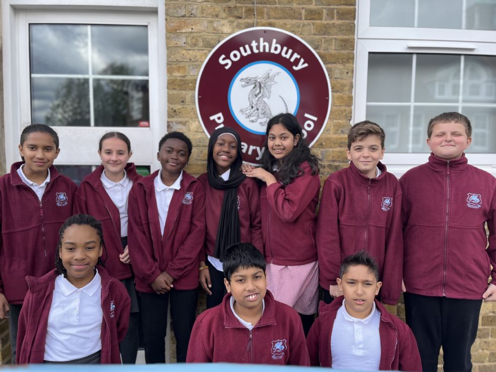 A group of children aged approximately 11 years old, wearing Southbury school uniform standing together ooutside the school office with the Southbury School sign behind them